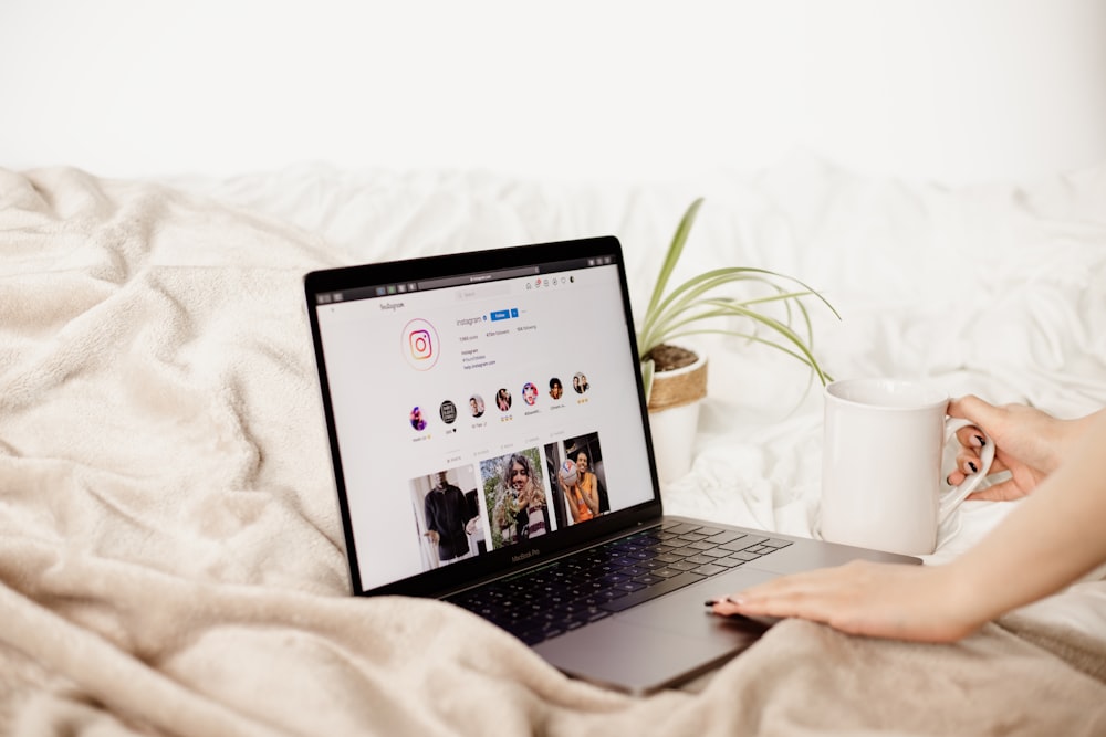 a woman is holding a coffee cup and looking at her laptop