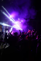 High-energy dance floor shot with strobe lights and hands raised in the air.
