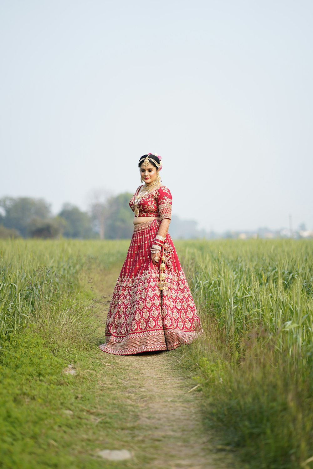 a woman in a red and pink lehenga standing in a field