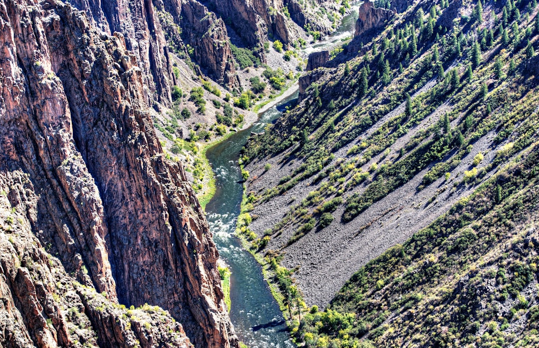 a river running through a canyon surrounded by mountains, Black Canyon of the Gunnison the River and the Cliffs</p>
<p></p>
<p>This is a view of the Gunnison River as it flows at the bottom of the canyon. The Black Canyon of the Gunnison has extremely steep cliff walls and some of the oldest rock in North America.</p>
<p>
