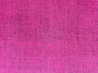 A textured fabric surface featuring a rich, deep pink color woven with visible threads creating a subtle pattern.