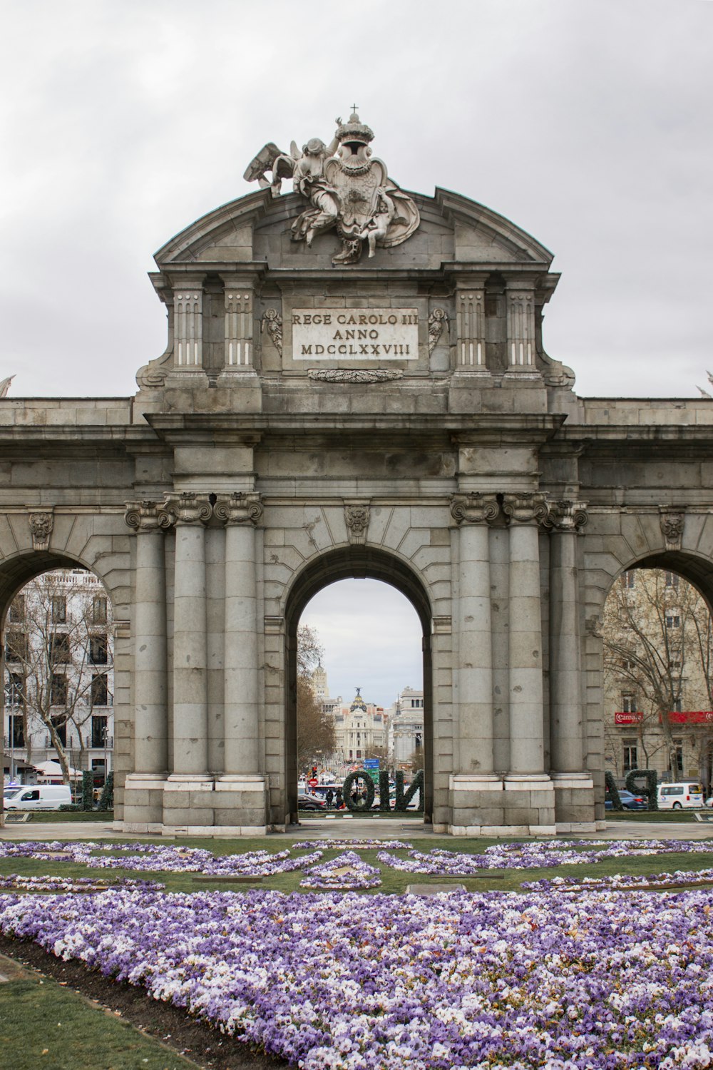 a large stone arch with a bunch of purple flowers in front of it