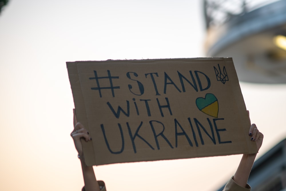 「ウクライナと共に立つ」と書かれた看板を持つ人