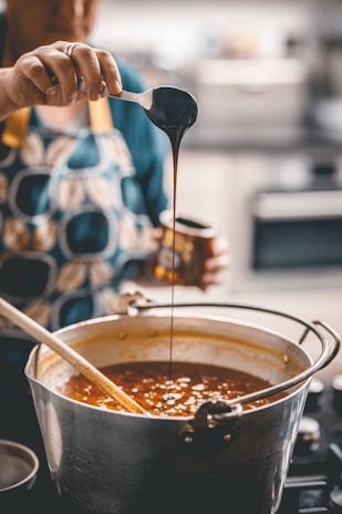 A close-up of hands using a vibrant enamel ladle to serve food from a pot.