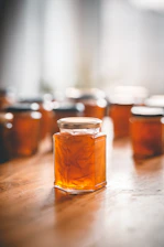 A rustic kitchen table with jars of vibrant marmalade surrounded by fresh fruits and a wooden spoon.