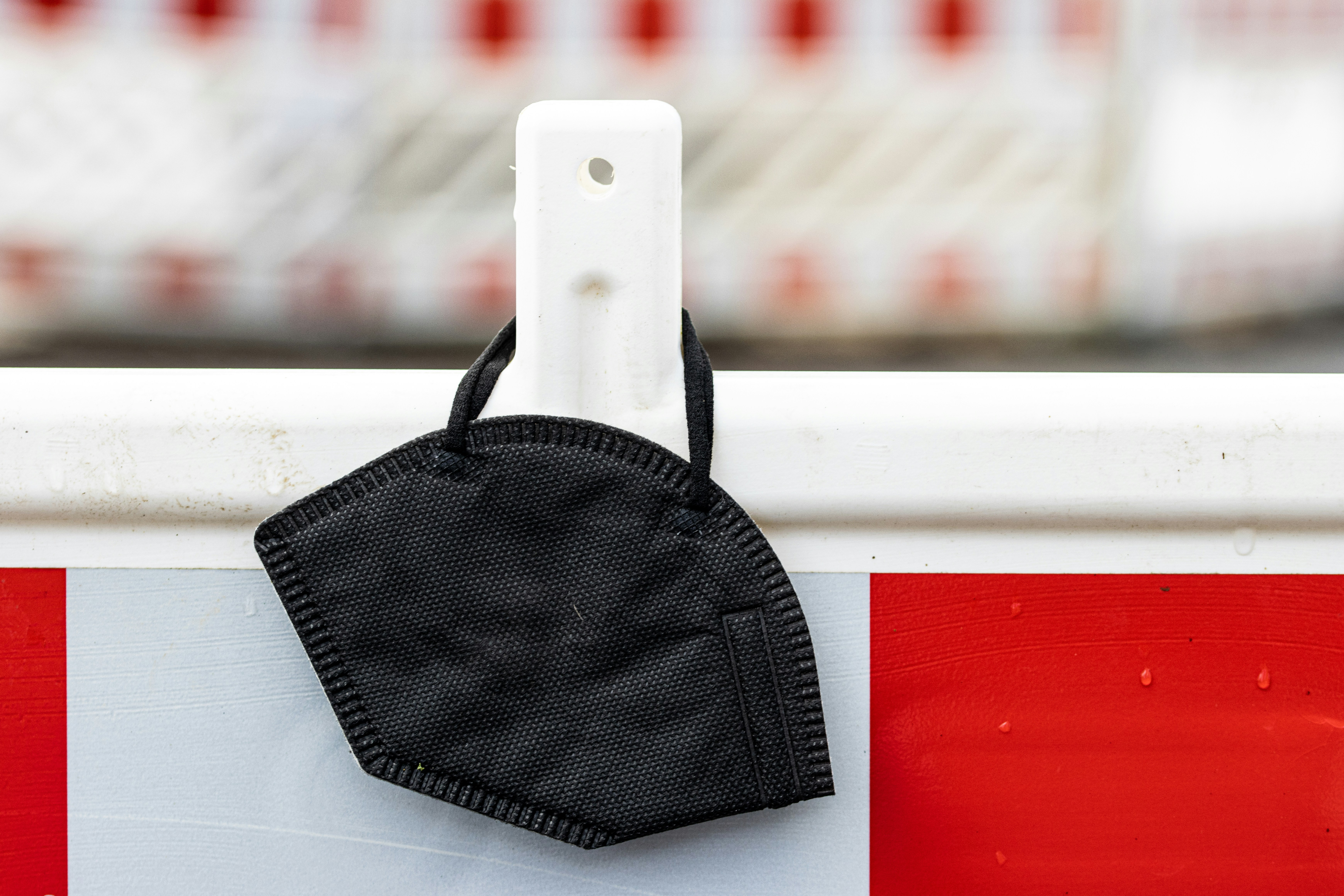 eine schwarze Gesichtsmaske, die an einer rot-weißen Barrikade hängt