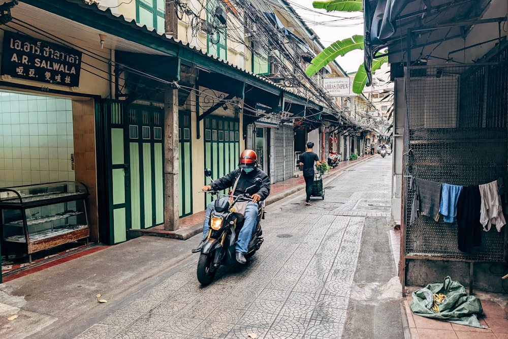 a man riding a motorcycle down a narrow street