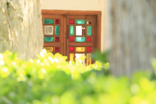 A close-up of a richly grained wooden door with colorful stained glass panels glowing in sunlight.