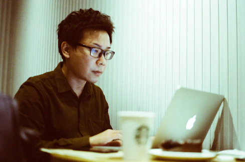 A focused doctoral student working on a laptop with notes and coffee nearby.
