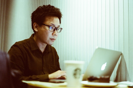 A focused learner working on a laptop with notes and coffee nearby.