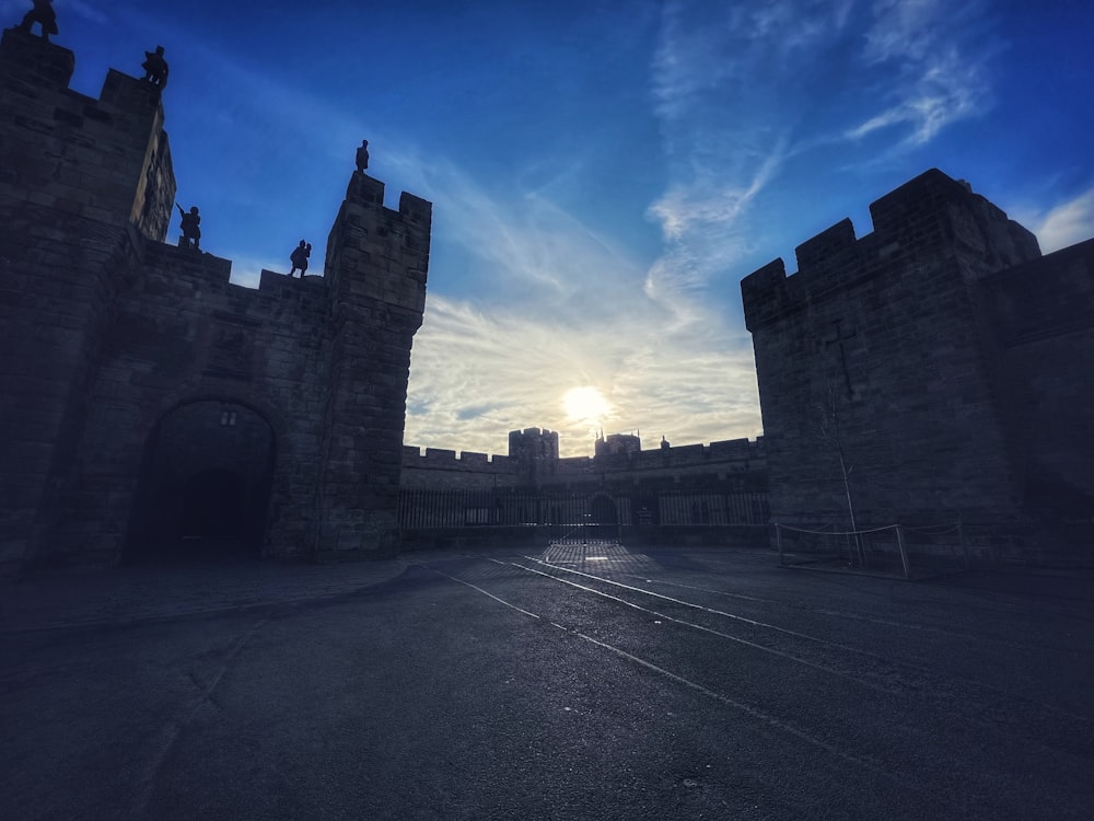 the sun is setting behind a castle gate