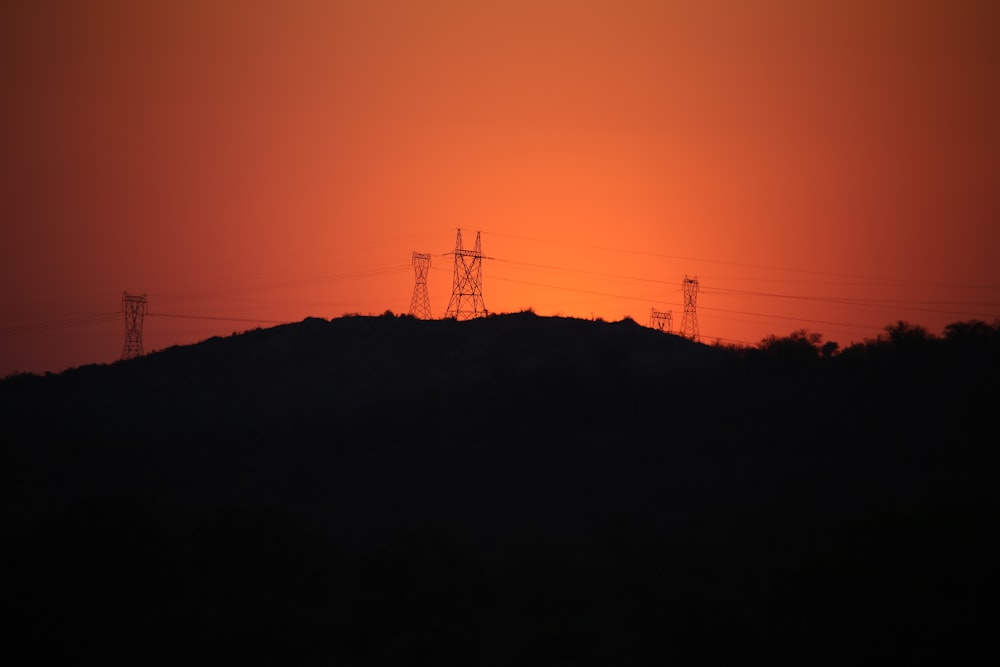 the sun is setting over a hill with power lines