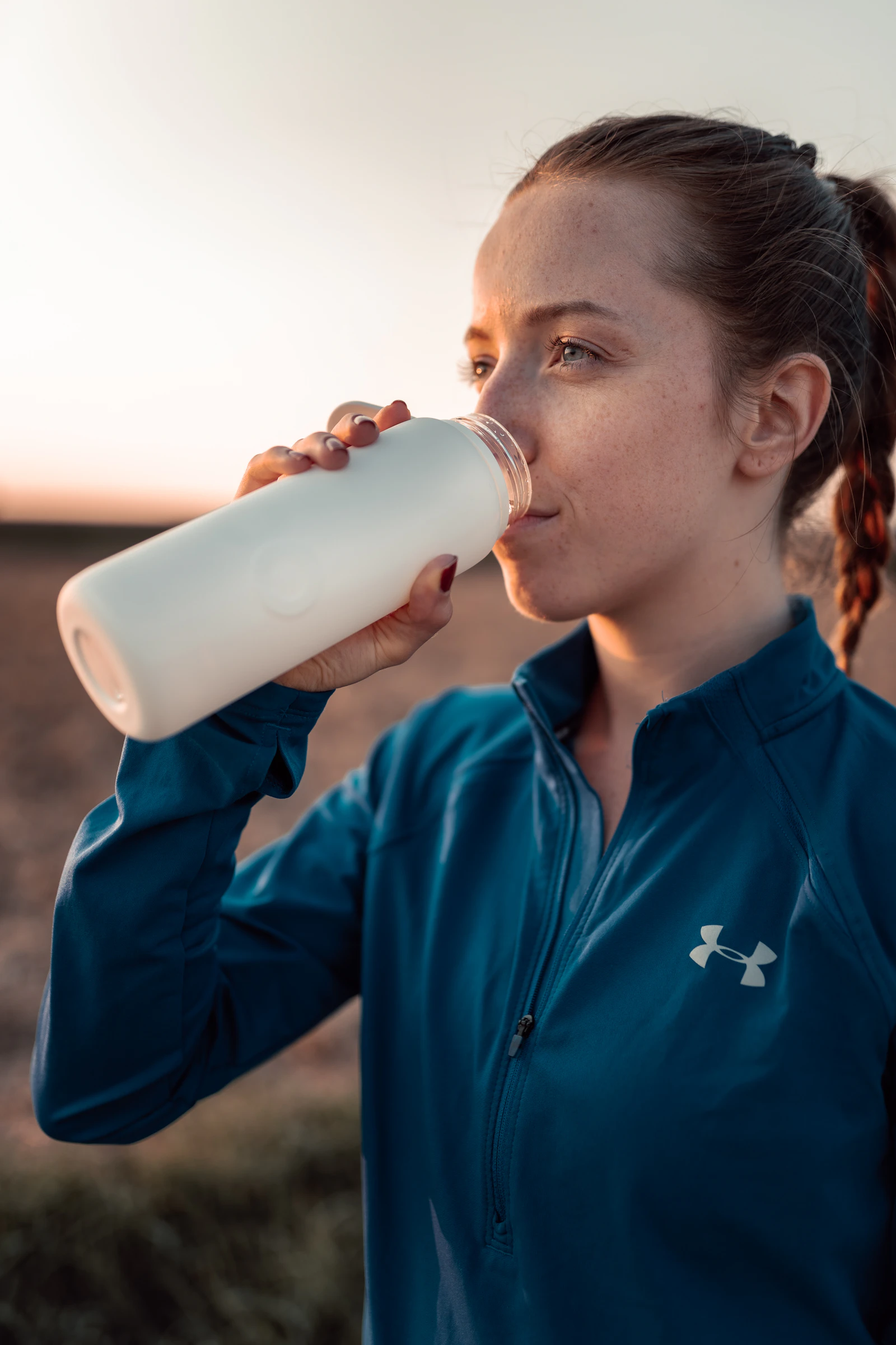 A woman in athletic wear drinks water from a reusable bottle after a workout.