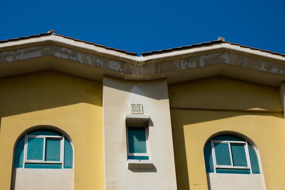 a yellow building with two windows and a blue sky in the background