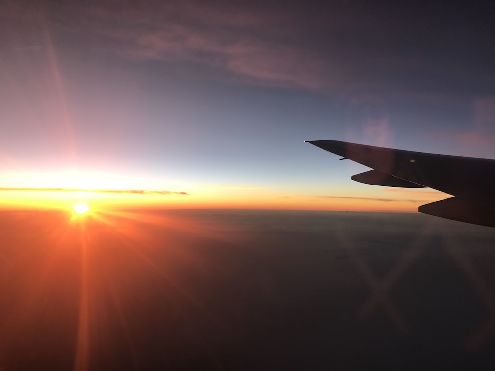 the sun is setting over the wing of an airplane