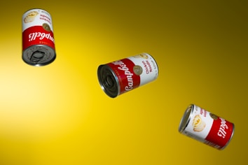 Three cans of Campbell's Chicken Noodle Soup are floating against a bright yellow background. The cans are positioned at different angles and appear to be suspended in mid-air, showcasing the familiar red and white label with the gold medallion design.