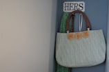 A colorful crossbody bag hanging from a rustic hook against a brick wall.