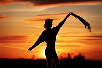 a silhouette of a woman holding a scarf in front of a sunset