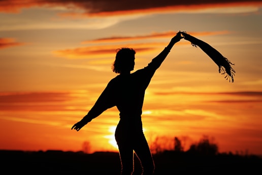 a silhouette of a woman holding a scarf in front of a sunset