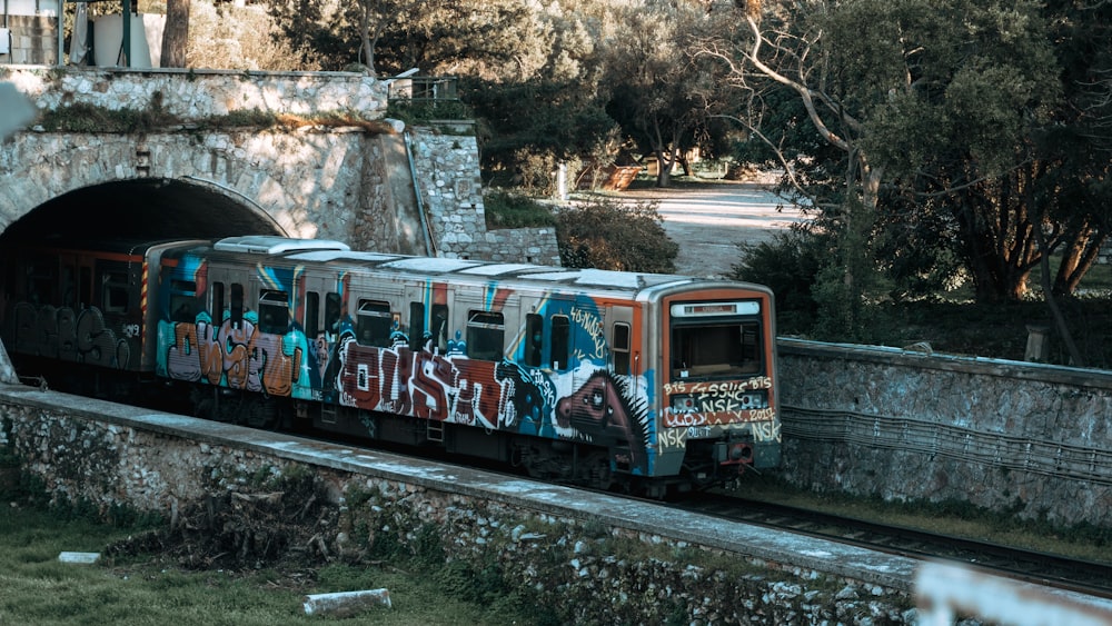 a train with graffiti on it passing under a bridge