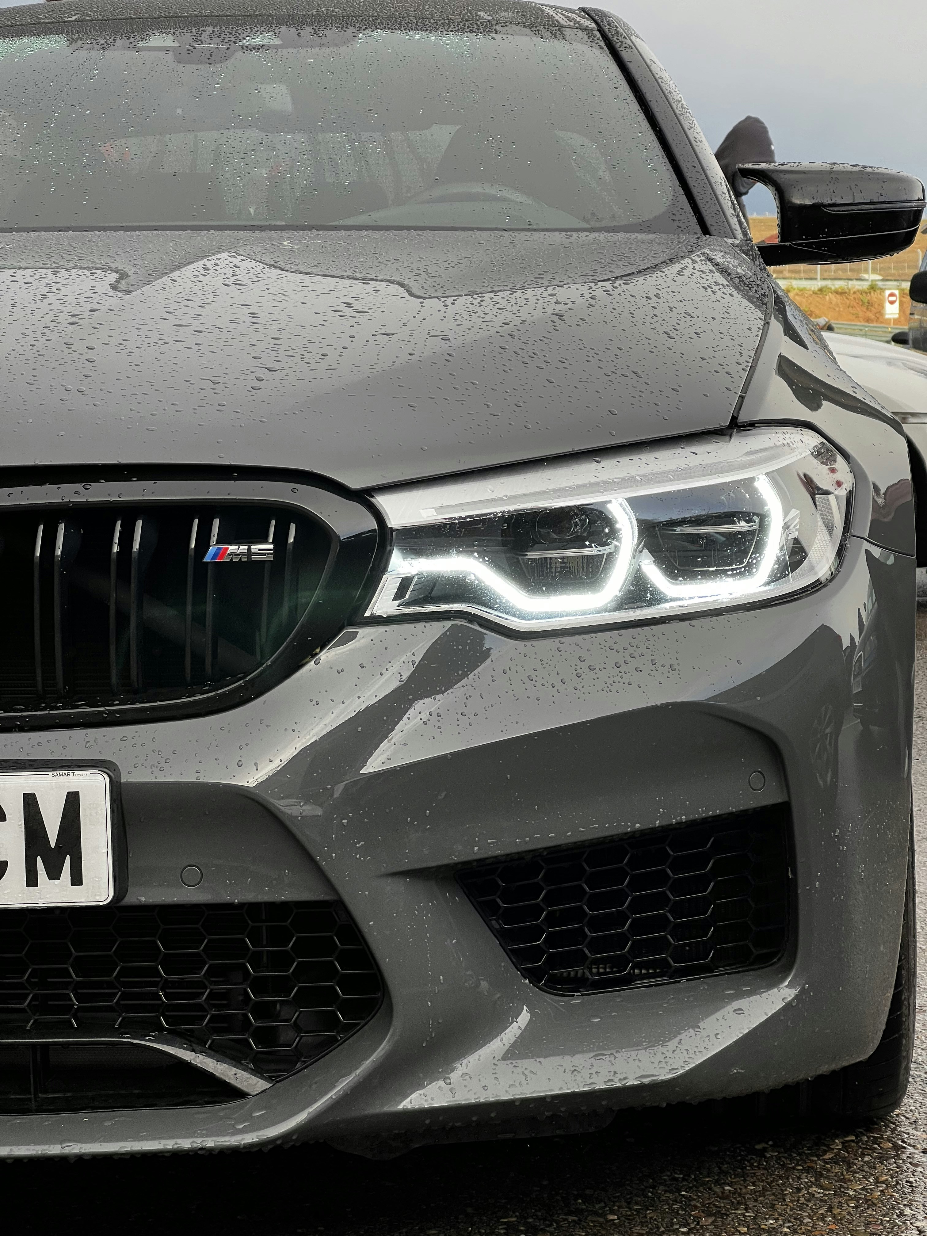 Dark gray BMW M5 sedan on urban highway at night, rain-slicked road, city glow
