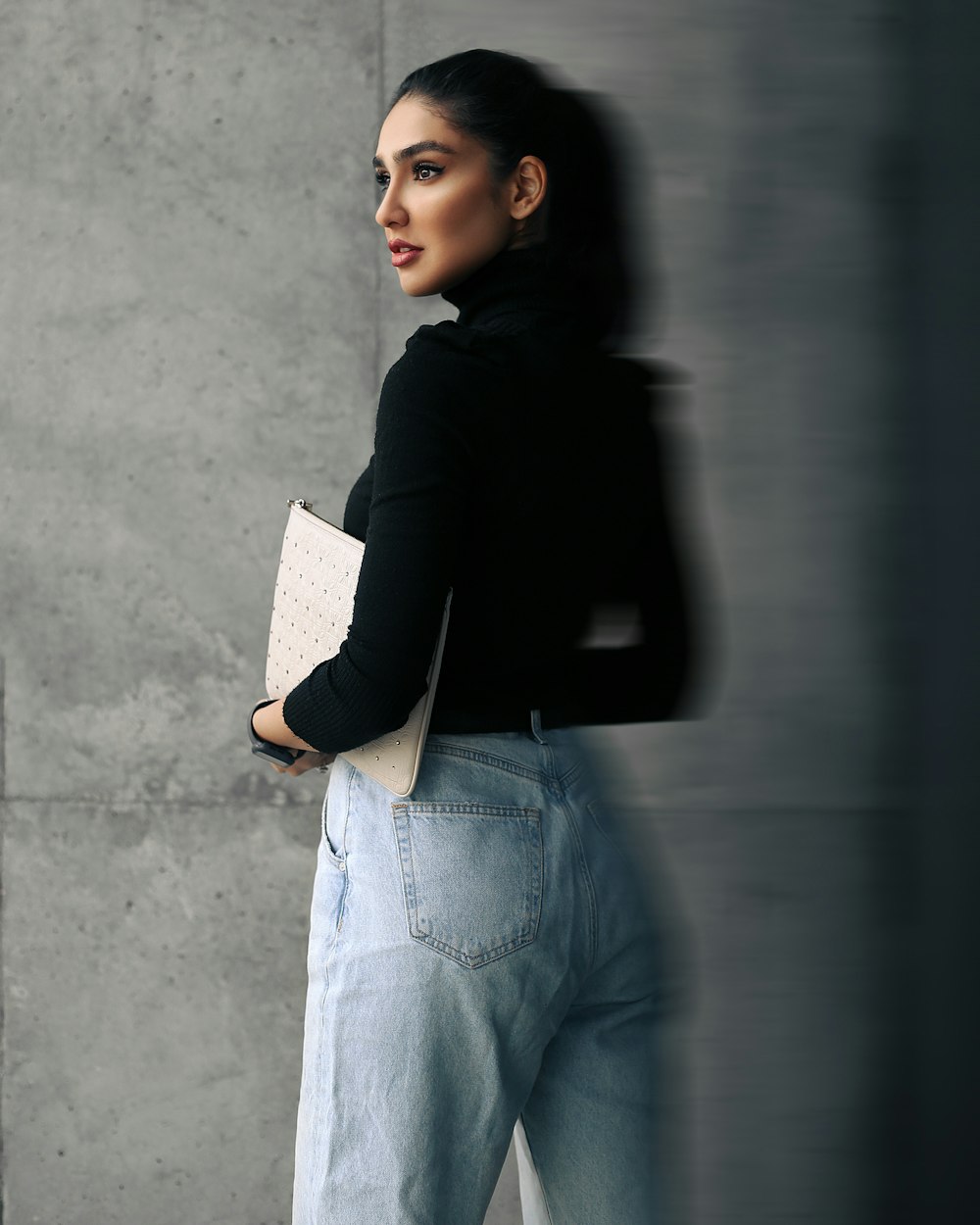 a woman in black jacket and jeans leaning against a wall