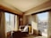 A cozy, sunlit hotel room with a large window overlooking the city skyline.