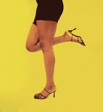 Close-up of a sophisticated woman’s foot stepping gracefully into a sleek, black stiletto against a softly lit background.