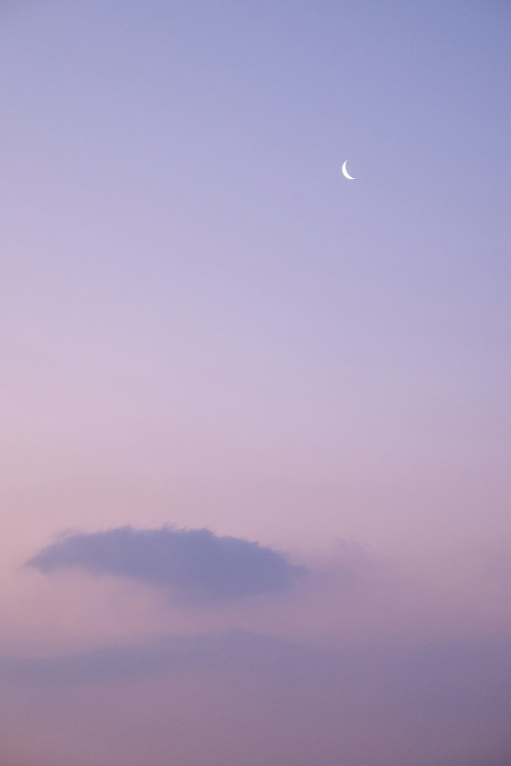 a cloud in the sky with a half moon in the distance