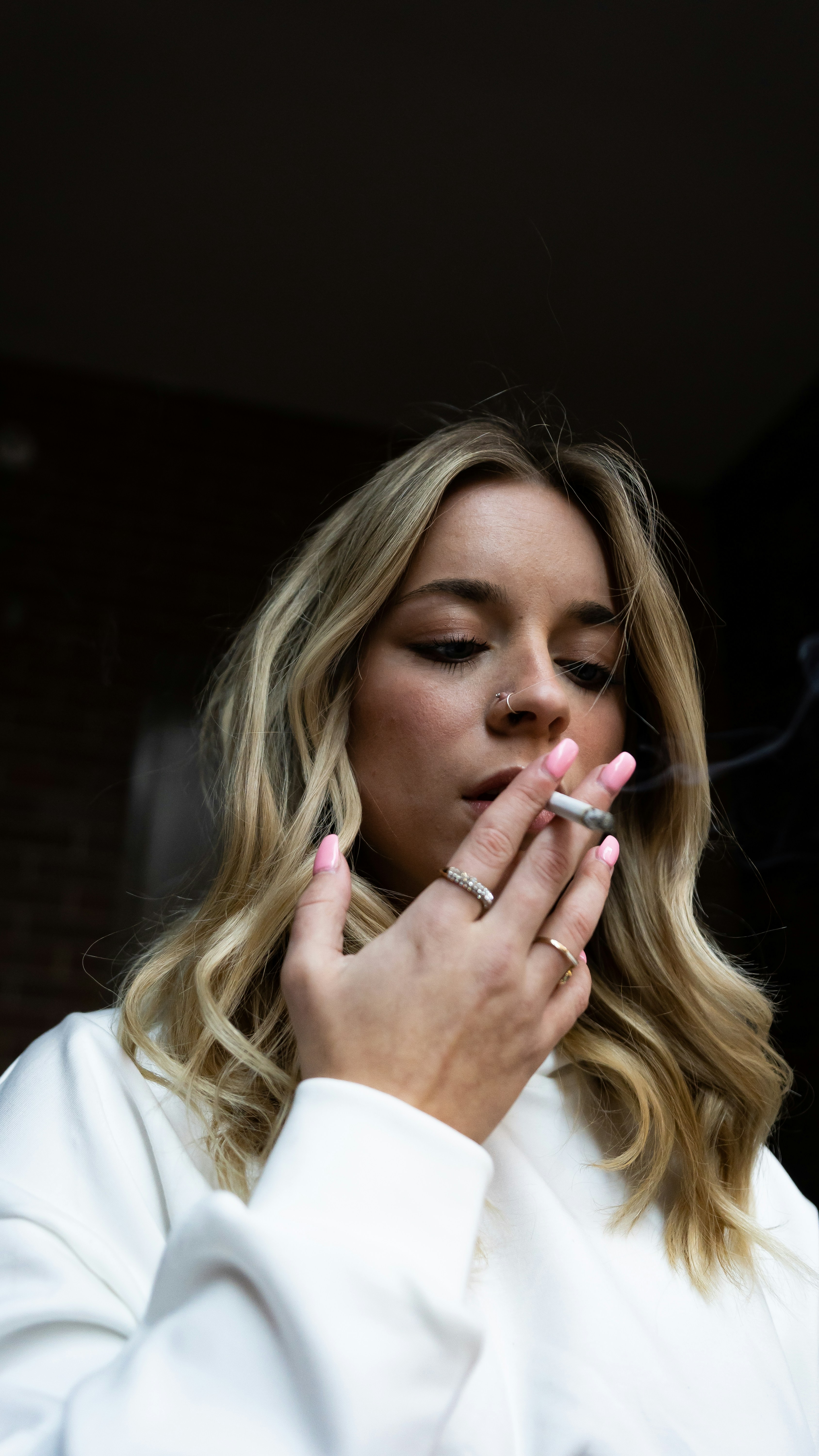 a woman smoking a cigarette in front of a brick wall