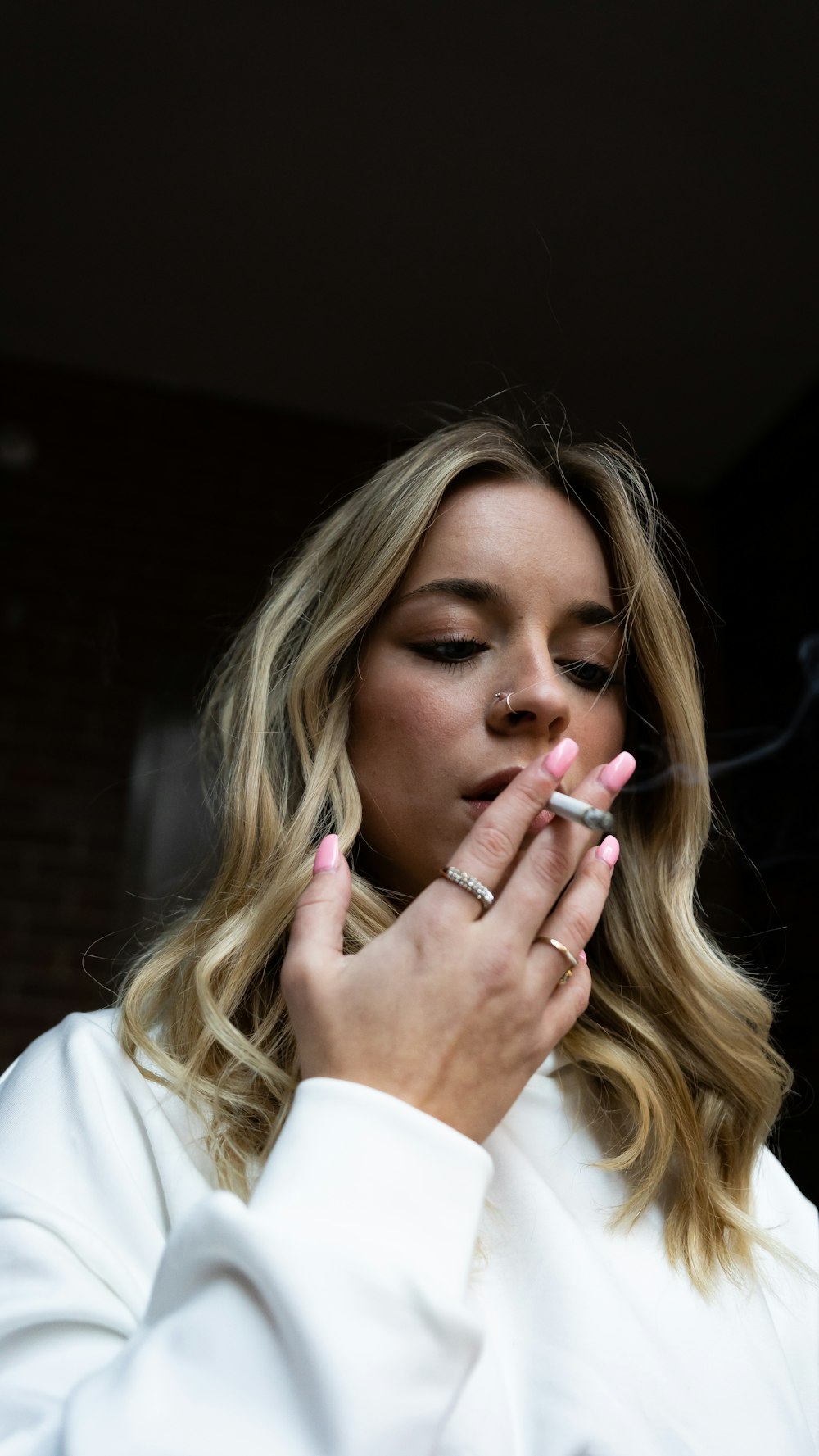 a woman smoking a cigarette in front of a brick wall