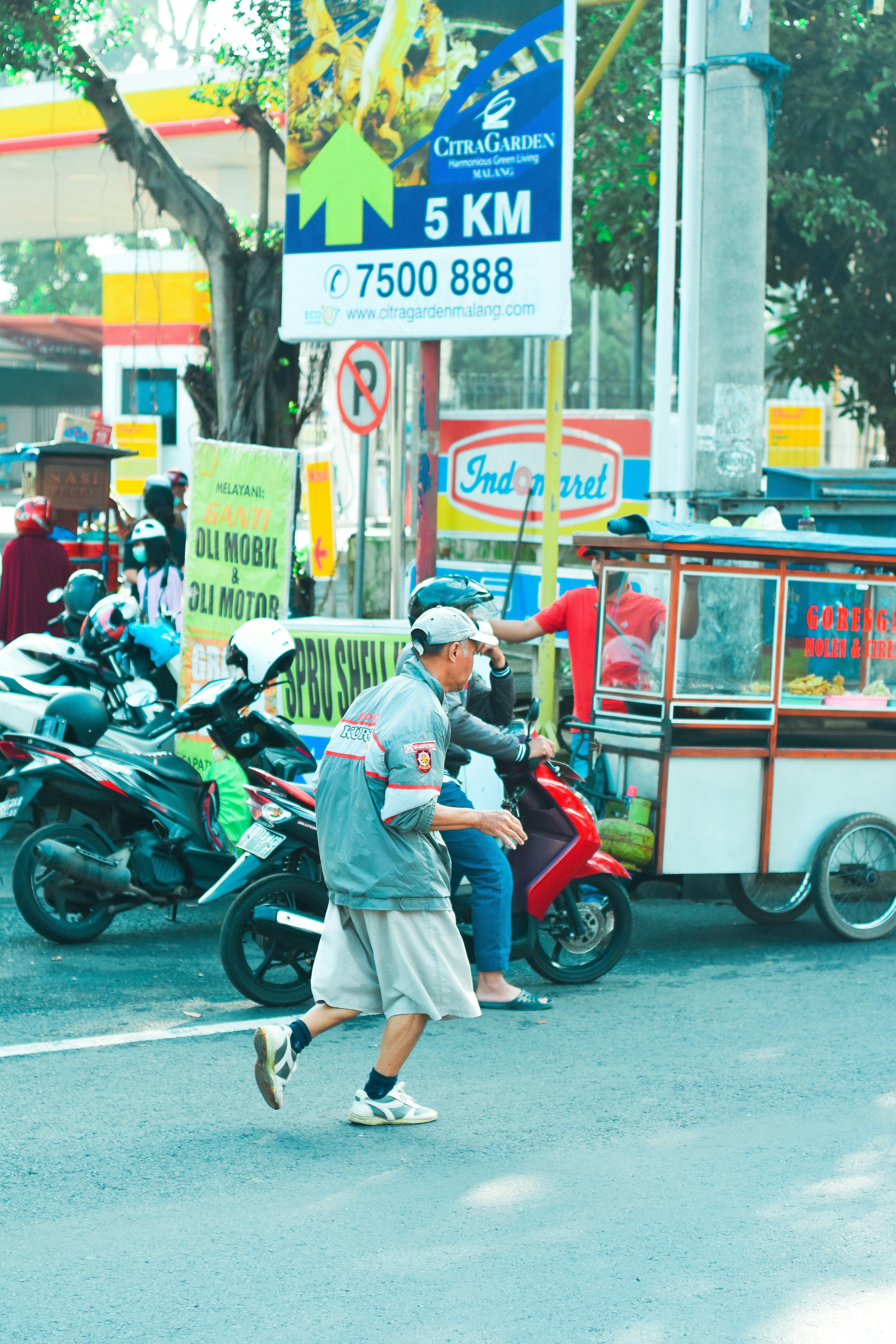 Seorang pria berjalan melintasi jalan di sebelah sepeda motor