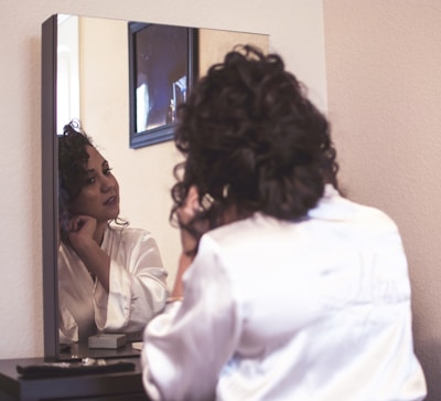 Close-up of a woman adjusting her elegant earrings in front of a mirror, her reflection showing quiet confidence.