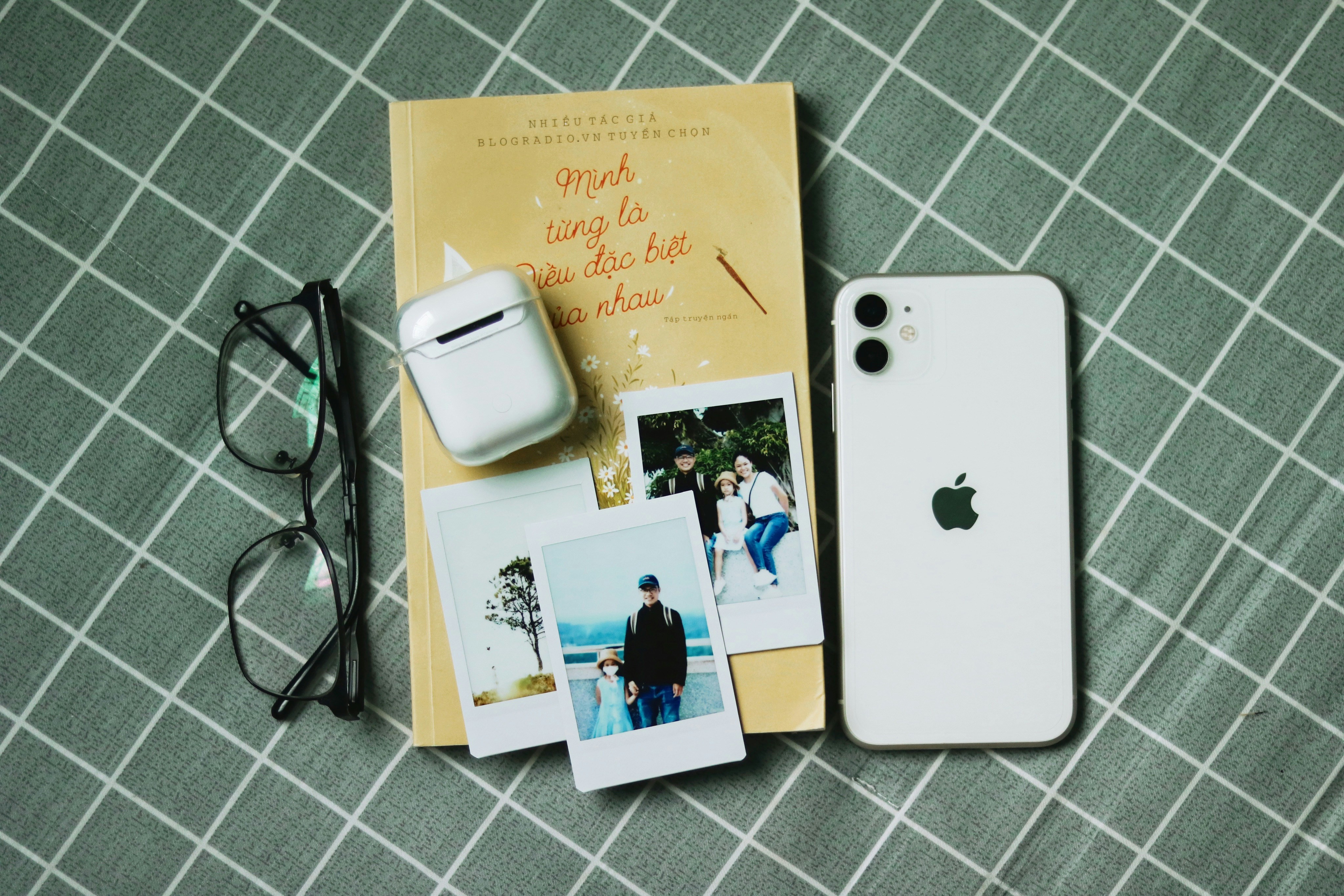 an iphone, book, and sunglasses on a bed