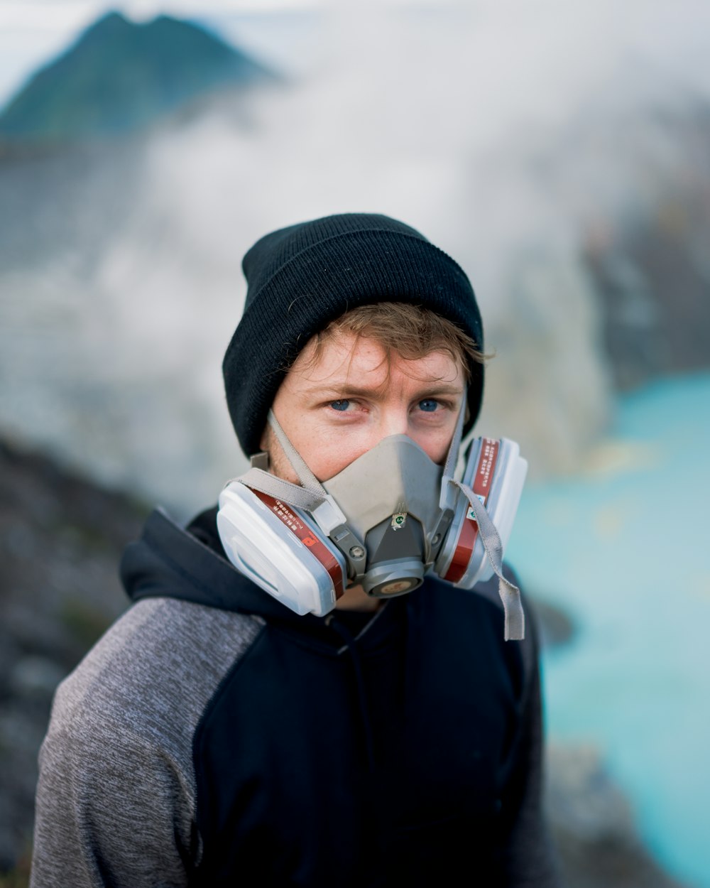 a man wearing a gas mask standing in front of a body of water