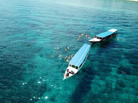 Two boats are floating on clear, turquoise waters. Several people in snorkel gear are swimming around the boats, enjoying the aquatic environment.