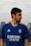 A person with a beard is wearing a blue sports jersey with the Real Madrid logo and sponsor branding. They are outdoors, with a blurred urban background and cloudy sky.
