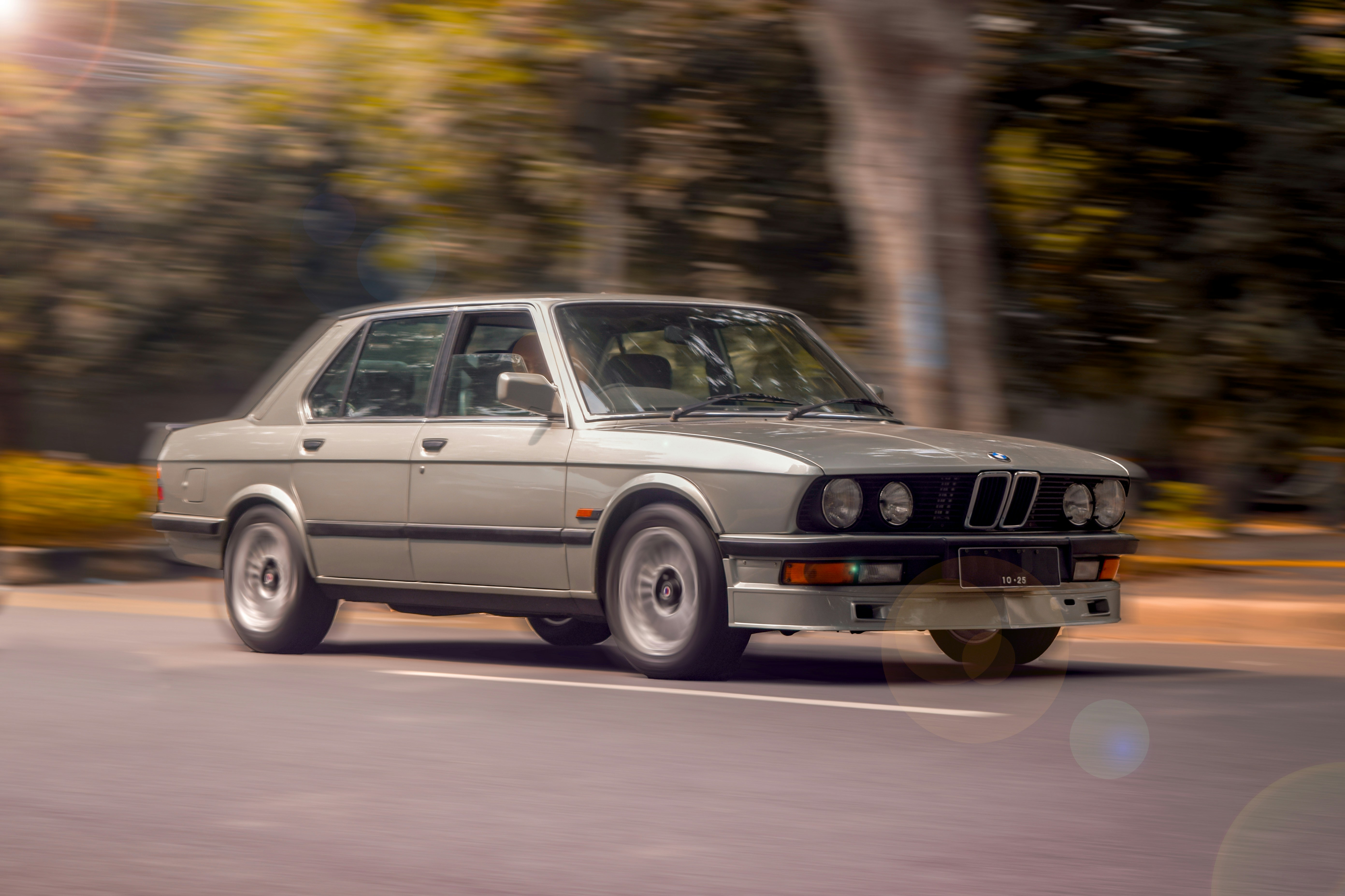 a silver car driving down a street next to trees
