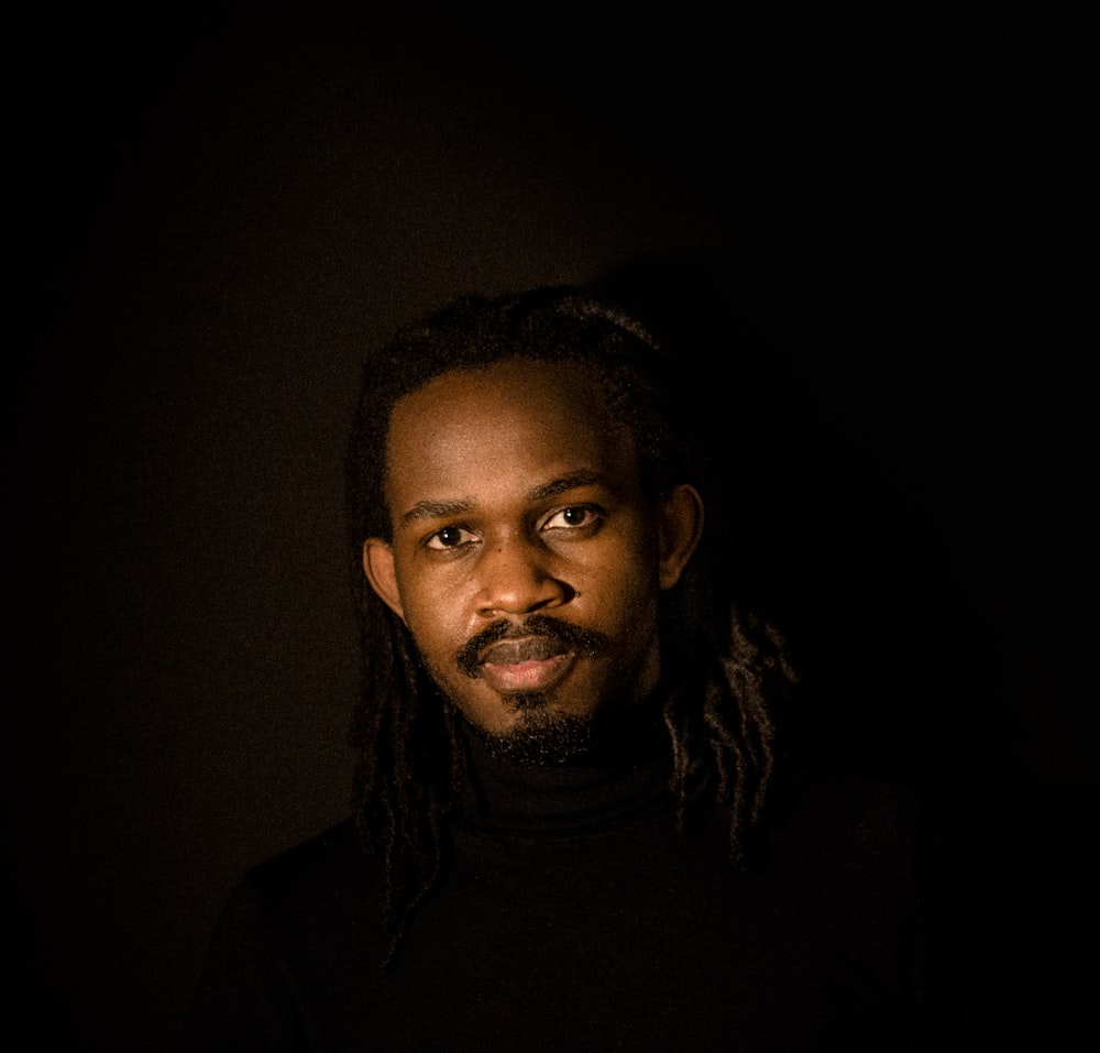a man with dreadlocks standing in a dark room