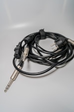 A coiled bundle of audio cables with different connectors, including a three-prong plug and an audio jack, placed on a smooth, light-colored surface.