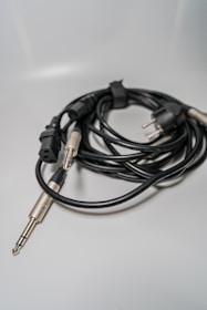 A coiled bundle of audio cables with different connectors, including a three-prong plug and an audio jack, placed on a smooth, light-colored surface.