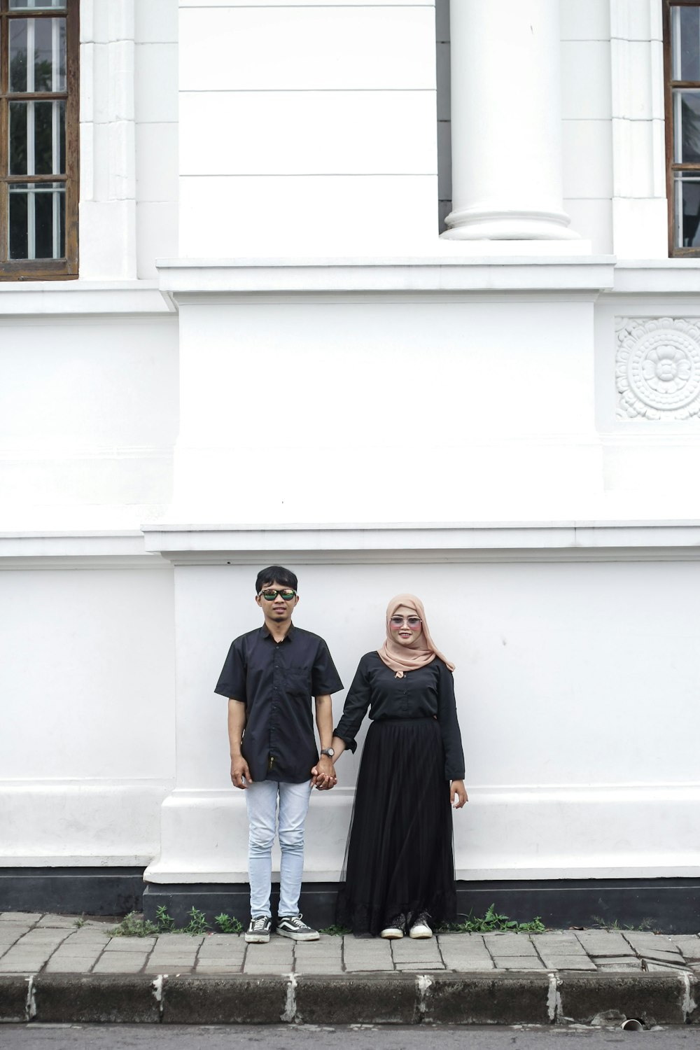 a man and woman standing next to each other in front of a white building