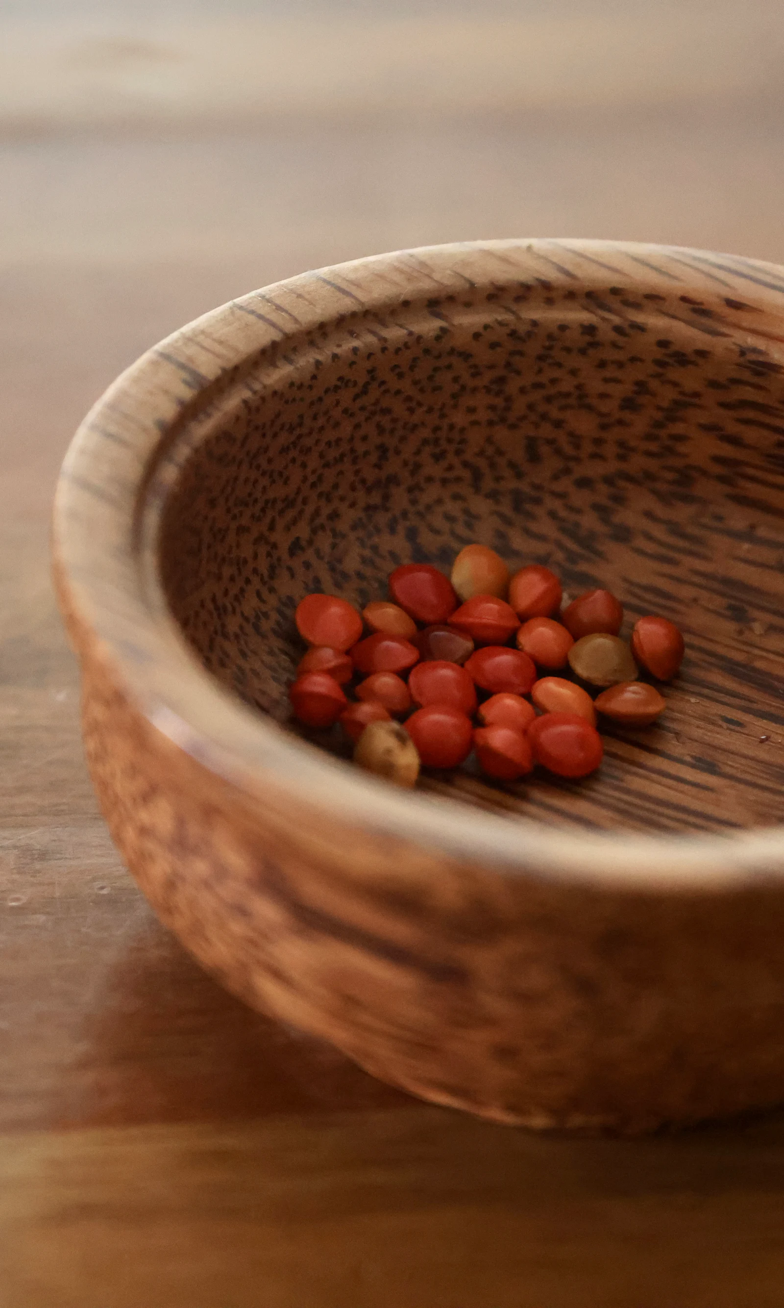 A wooden bowl of nuts standing on a scrubbed wooden table.
