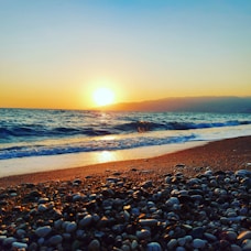 the sun is setting over the ocean on the beach