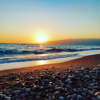 the sun is setting over the ocean on the beach
