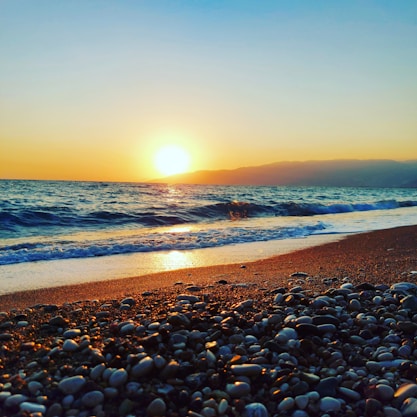 the sun is setting over the ocean on the beach