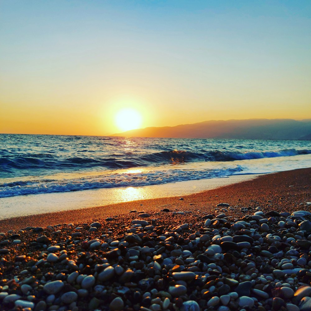 the sun is setting over the ocean on the beach