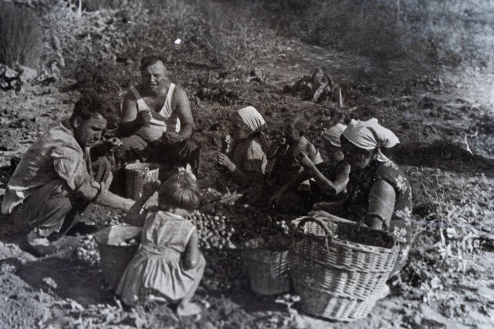 a group of people sitting around a basket filled with fruit