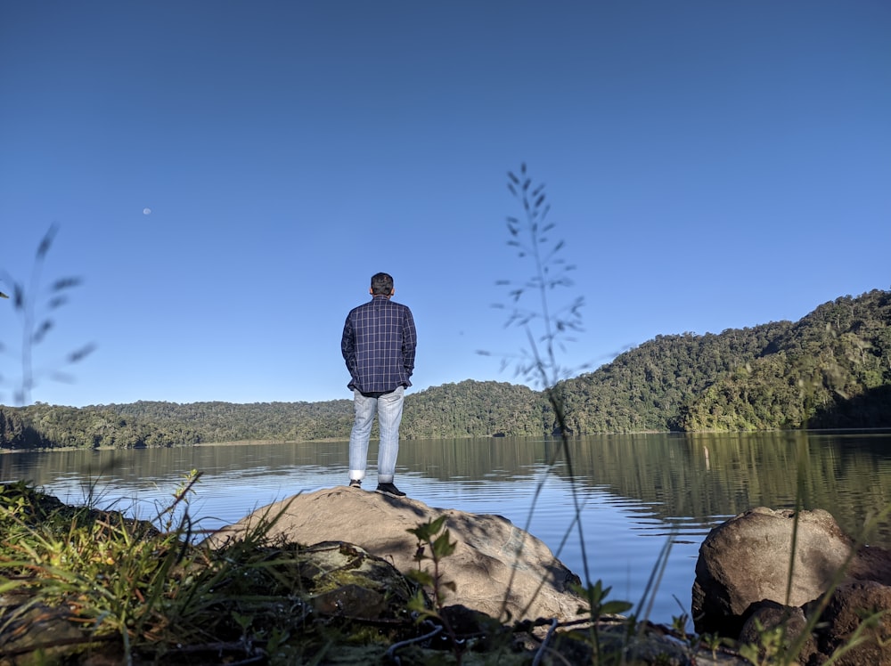 a man standing on top of a rock next to a body of water