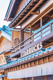 A modern coffee shop blends traditional architectural elements with contemporary branding. Wooden structures with intricate details reflect classic design, while the familiar coffee shop logo and sign add a modern contrast.